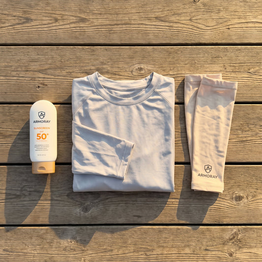 Flat lay of a sunscreen bottle, folded UPF shirt, and arm sleeves on a wooden outdoor deck.