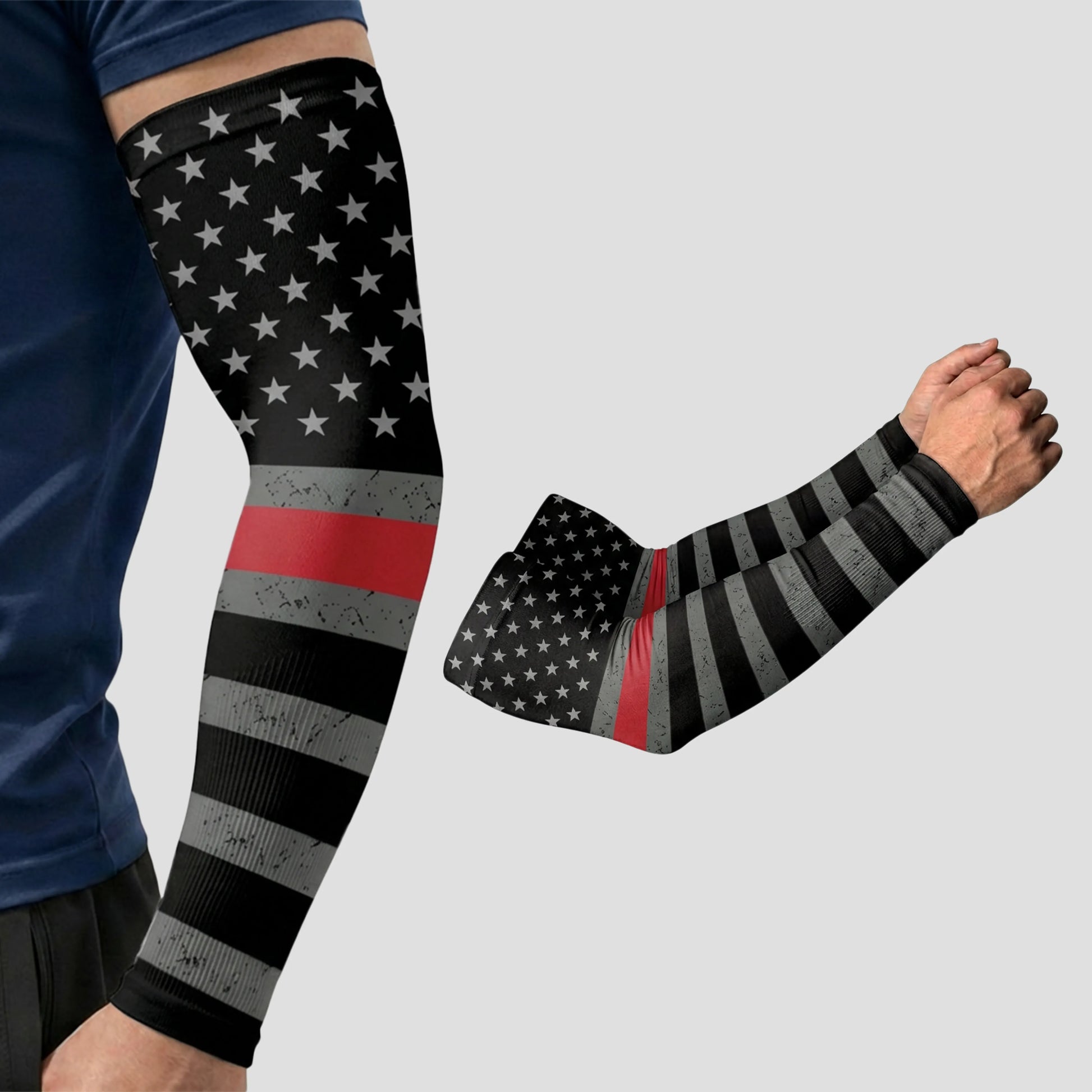 A person wears an ARMORAY Armoray® Patterned Arm Sleeve featuring a black and gray American flag design with a single thin red line, providing UPF 50+ sun protection. Another view of the sleeve is shown on the right.