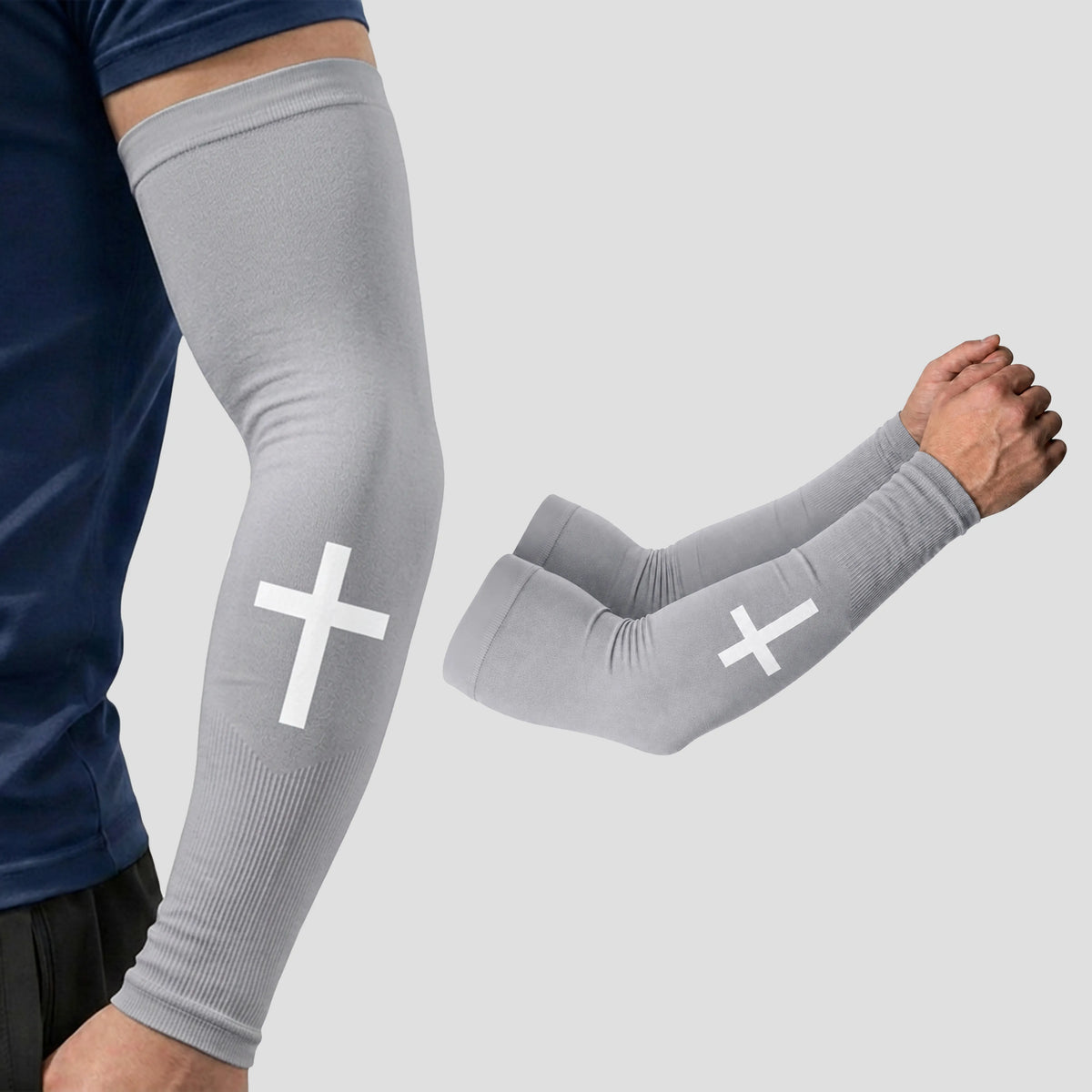 A person is wearing ARMORAY Faith Series gray compression arm sleeves with a white cross design, offering UPF 50+ sun protection for reliable coverage; a separate pair of these moisture-wicking sleeves is also displayed on a light gray background.