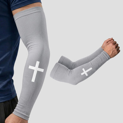 A person is wearing ARMORAY Faith Series gray compression arm sleeves with a white cross design, offering UPF 50+ sun protection for reliable coverage; a separate pair of these moisture-wicking sleeves is also displayed on a light gray background.