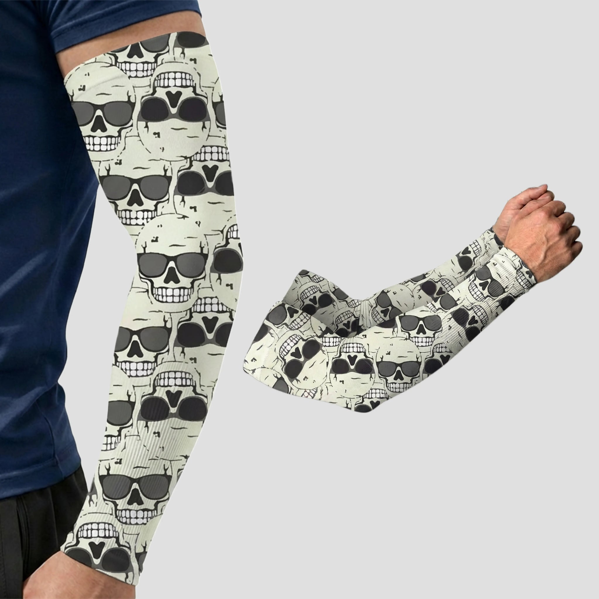 A man wearing an Armoray® Patterned Arm Sleeve by ARMORAY, featuring a bold black and white skull print; a second matching sleeve—designed for UPF 50+ sun protection—is displayed beside him on a plain background.