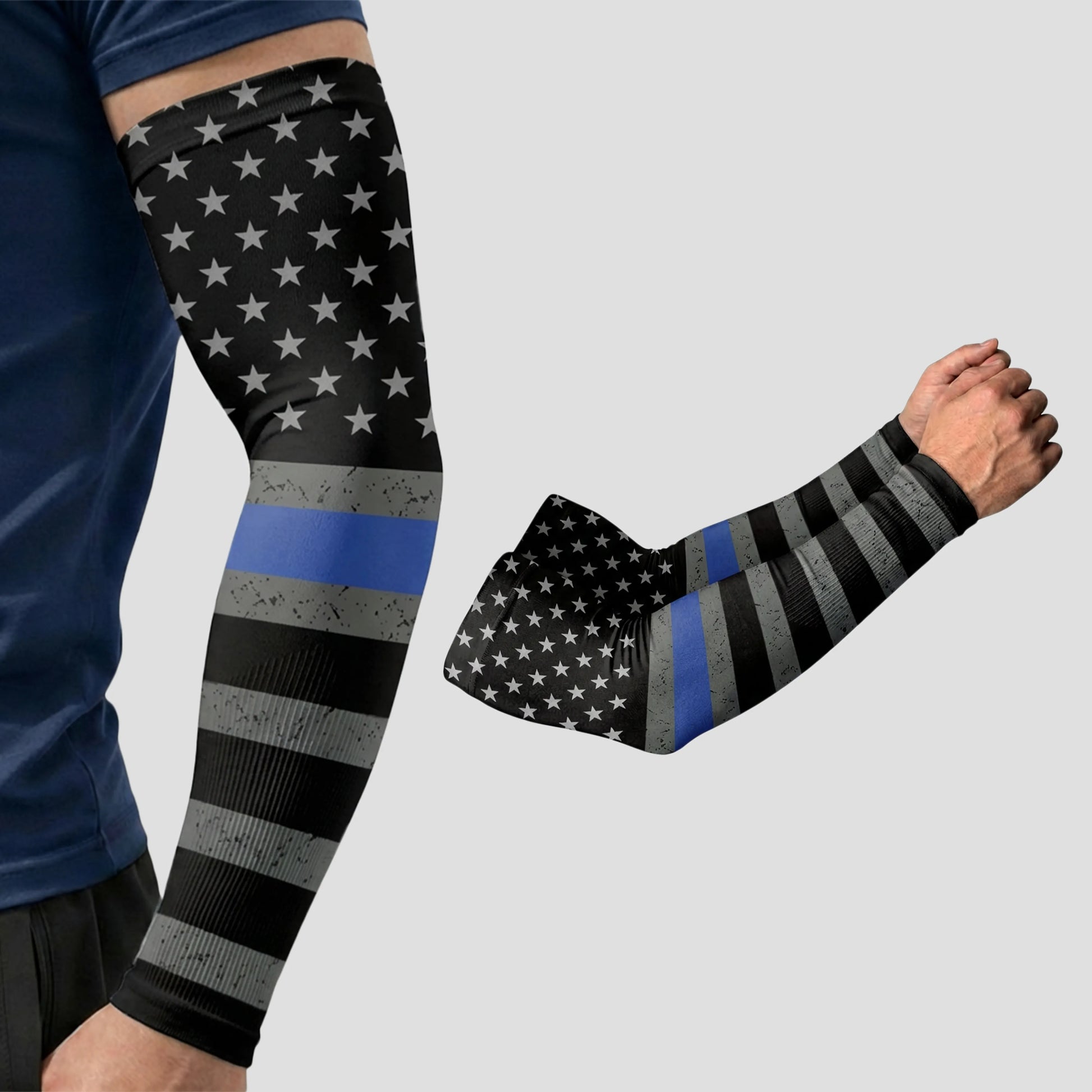 A person is wearing an ARMORAY Armoray® Patterned Arm Sleeve in a black, white, and gray American flag design with a single blue line. Crafted from UPF 50+ fabric for superior sun protection, the set includes a second sleeve displayed alongside the arm.