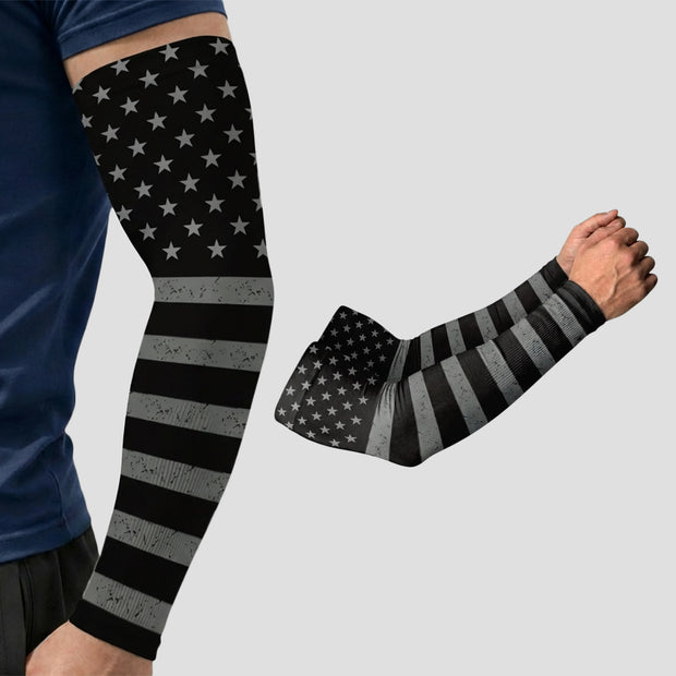 A person wearing an Armoray® Patterned Arm Sleeve by ARMORAY, featuring a black and gray American flag design and UPF 50+ sun protection, with a second sleeve displayed separately on a gray background.