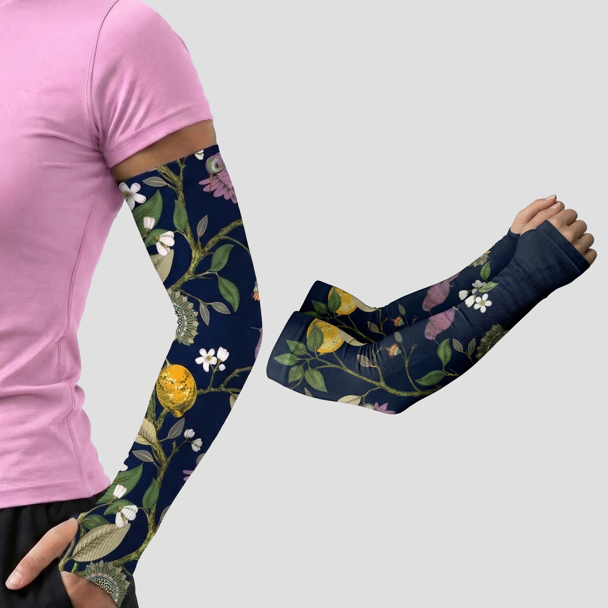 A person in a pink shirt wears an ARMORAY Armoray® Garden Collection Arm Sleeve — Designed to Delight Outdoors, featuring a floral-patterned navy design; beside them, a separate image shows the same UPF 50+ sun protection sleeve from the collection on a bent arm, both displayed against a plain gray background.
