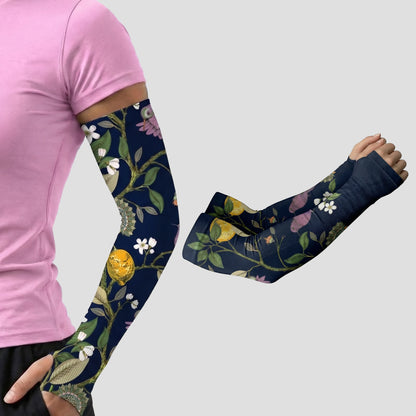 A person in a pink shirt wears an ARMORAY Armoray® Garden Collection Arm Sleeve — Designed to Delight Outdoors, featuring a floral-patterned navy design; beside them, a separate image shows the same UPF 50+ sun protection sleeve from the collection on a bent arm, both displayed against a plain gray background.