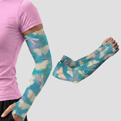 A person wears an ARMORAY Armoray® Garden Collection Arm Sleeve — Designed to Delight Outdoors, featuring a turquoise butterfly pattern, with a second matching sleeve displayed nearby; both provide UPF 50+ sun protection against a plain gray background.