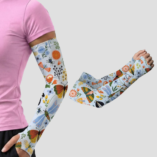Wearing ARMORAY Armoray® Garden Collection Arm Sleeves — Designed to Delight Outdoors, featuring UPF 50+ sun protection and vibrant floral and butterfly patterns, a person stands against a plain light gray background.