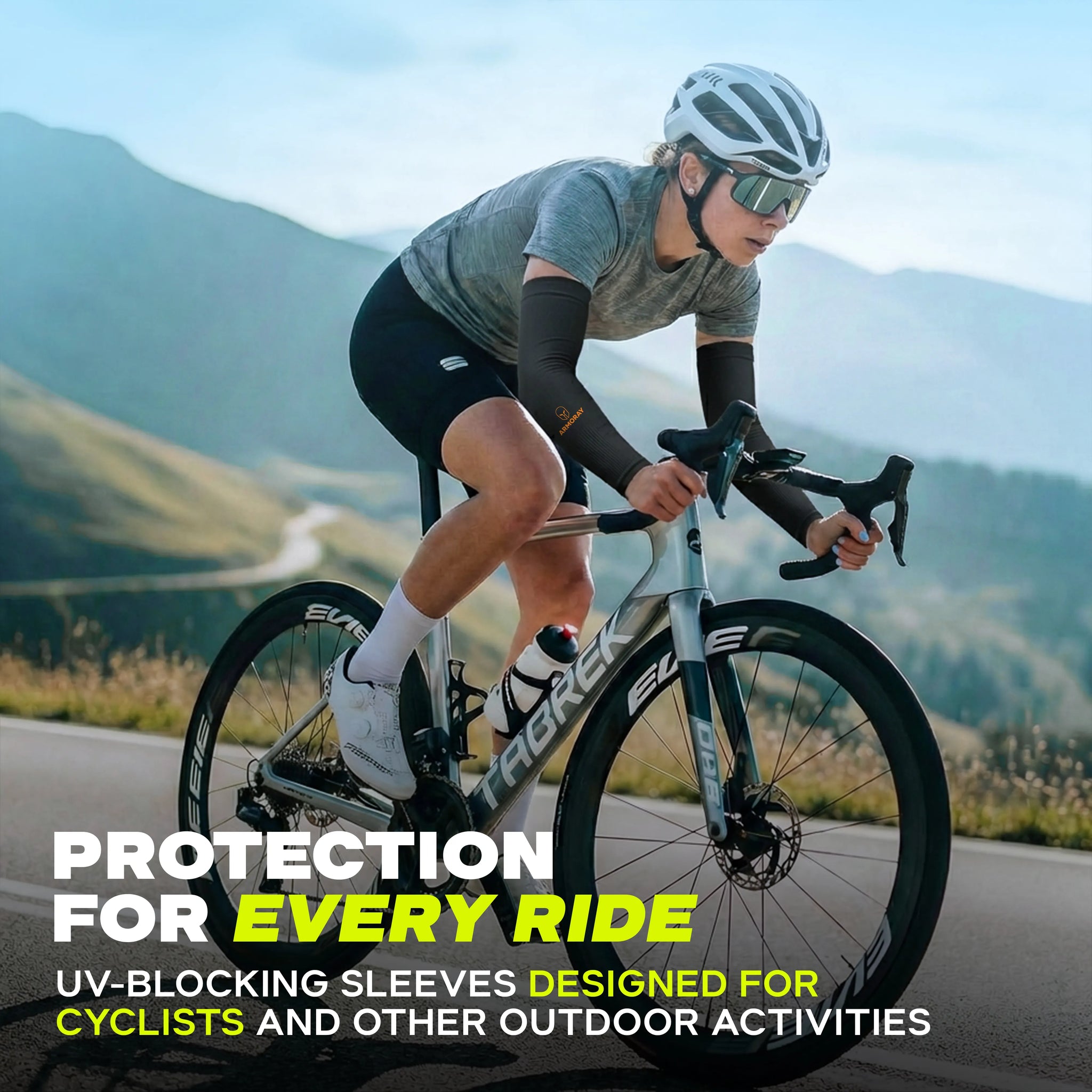 A cyclist wearing ARMORAY Armoray® Classic Arm Sleeves rides a road bike along a paved mountain road with rolling hills and a clear blue sky in the background. Overlayed text highlights how cyclists can stay cool and protected on their rides with Armoray® Classic Arm Sleeves.
