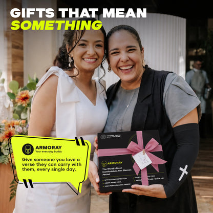 Two women smiling at an event; one holds a boxed Faith Series gift set from ARMORAY adorned with a pink ribbon and product description, highlighting features like UPF 50+ sun protection and moisture wicking for all-day comfort.
