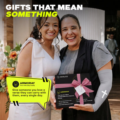 Two smiling women stand together; one holds a boxed gift with a pink bow and a yellow message card that reads, "Give someone you love a verse they can carry with them, every single day." The thoughtful package features ARMORAY’s Faith Series—a scripture sleeve: an inspiring, no-slip arm sleeve designed for comfort and style.