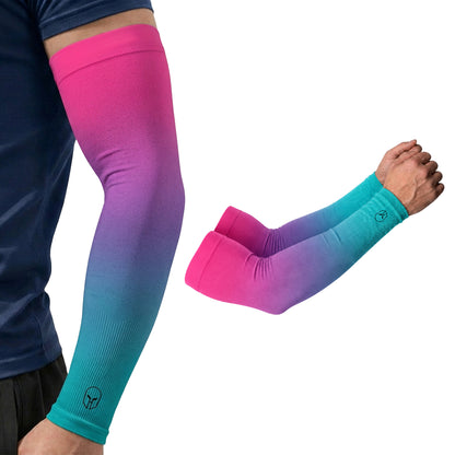 A person is wearing an ARMORAY Ombré Collection arm sleeve featuring a pink-to-blue gradient; next to the arm is a separate, matching pair of UPF 50+ sleeves from the same collection, providing UV protection.